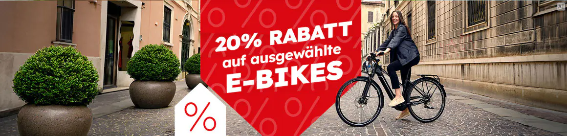 „20% Rabatt auf ausgewählte E-Bikes“: Frau fährt mit einem schwarzen E-Bike durch eine städtische Straße.