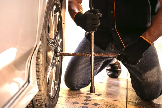 Mann kniet am Auto und löst mit einem Kreuzschlüssel die Radmuttern eines Autoreifens.