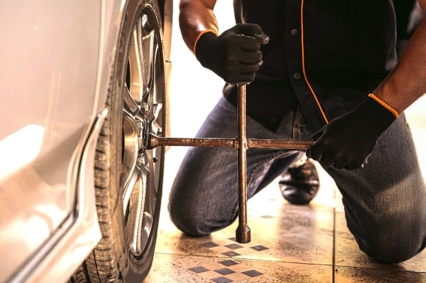 Mann kniet am Auto und löst mit einem Kreuzschlüssel die Radmuttern eines Autoreifens.