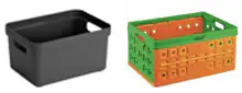 Zwei stapelbare Kunststoffboxen nebeneinander: links eine schwarze Box mit Grifföffnung, rechts eine klappbare orange-grüne Kiste.