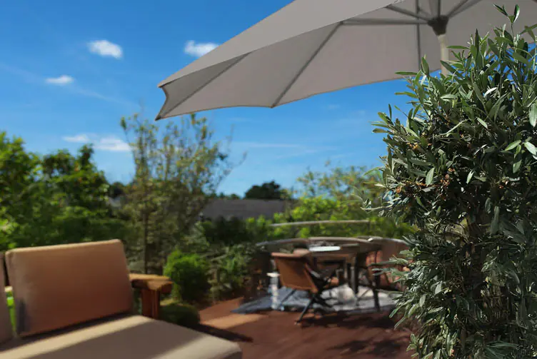 Terrasse mit Sitzmöbeln unter einem großen Sonnenschirm an einem sonnigen Tag, umgeben von Pflanzen und blauem Himmel.