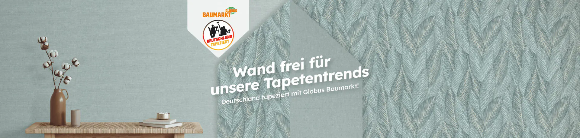 Raumszene mit blauer Blättertapete, Sideboard und Vase. Text: Wand frei für unsere Tapetentrends. Deutschland tapeziert mit Globus Baumarkt!
