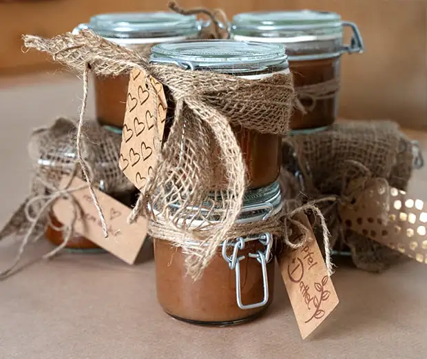 Mehrere kleine Einmachgläser mit selbstgemachter Apfel-Dattel-Marmelade, liebevoll dekoriert mit Jutestoff, Schnur und handgeschriebenen Etiketten. Auf den Etiketten steht "mit Liebe gemacht" und "Apfel Dattel".