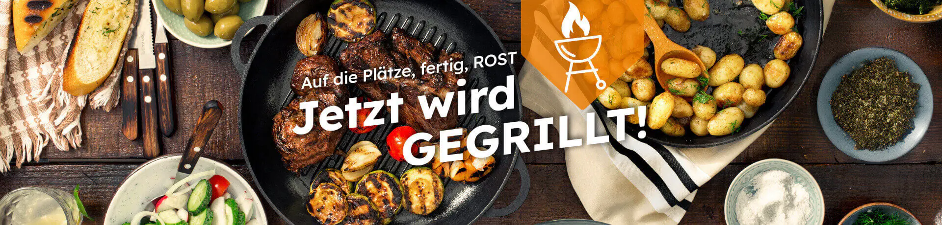 Jetzt wird gegrillt mit dem Text Auf die Plätze fertig Rost Grillpfanne mit Fleisch Gemüse und Beilagen auf einem Tisch angerichtet.