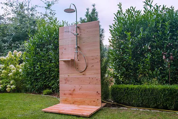 Auf einer Wiese steht eine Gartendusche aus Holz. 