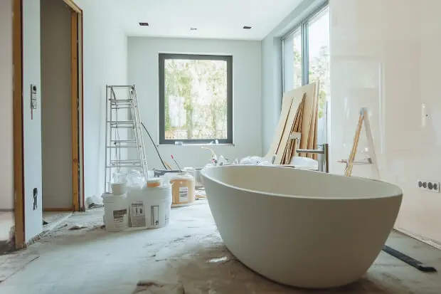 Modernes Badezimmer in Renovierung mit freistehender Badewanne, Farbeimern, Leiter und Baumaterialien auf dem Boden.  