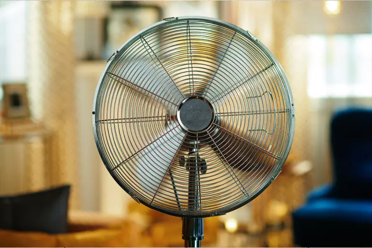 Großer Standventilator in einem Wohnraum als Abkühlung bei Hitze mit unscharfem Hintergrund und warmer Beleuchtung.